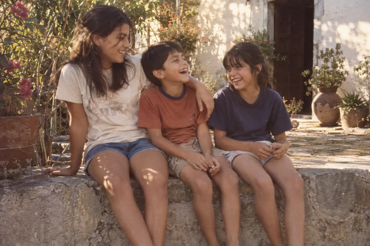 Tres hermanos sentados en un muro del patio, riéndose juntos.