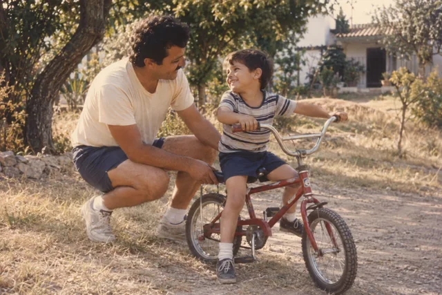 Un padre sostiene la bicicleta de su hijo mientras se sonríen.